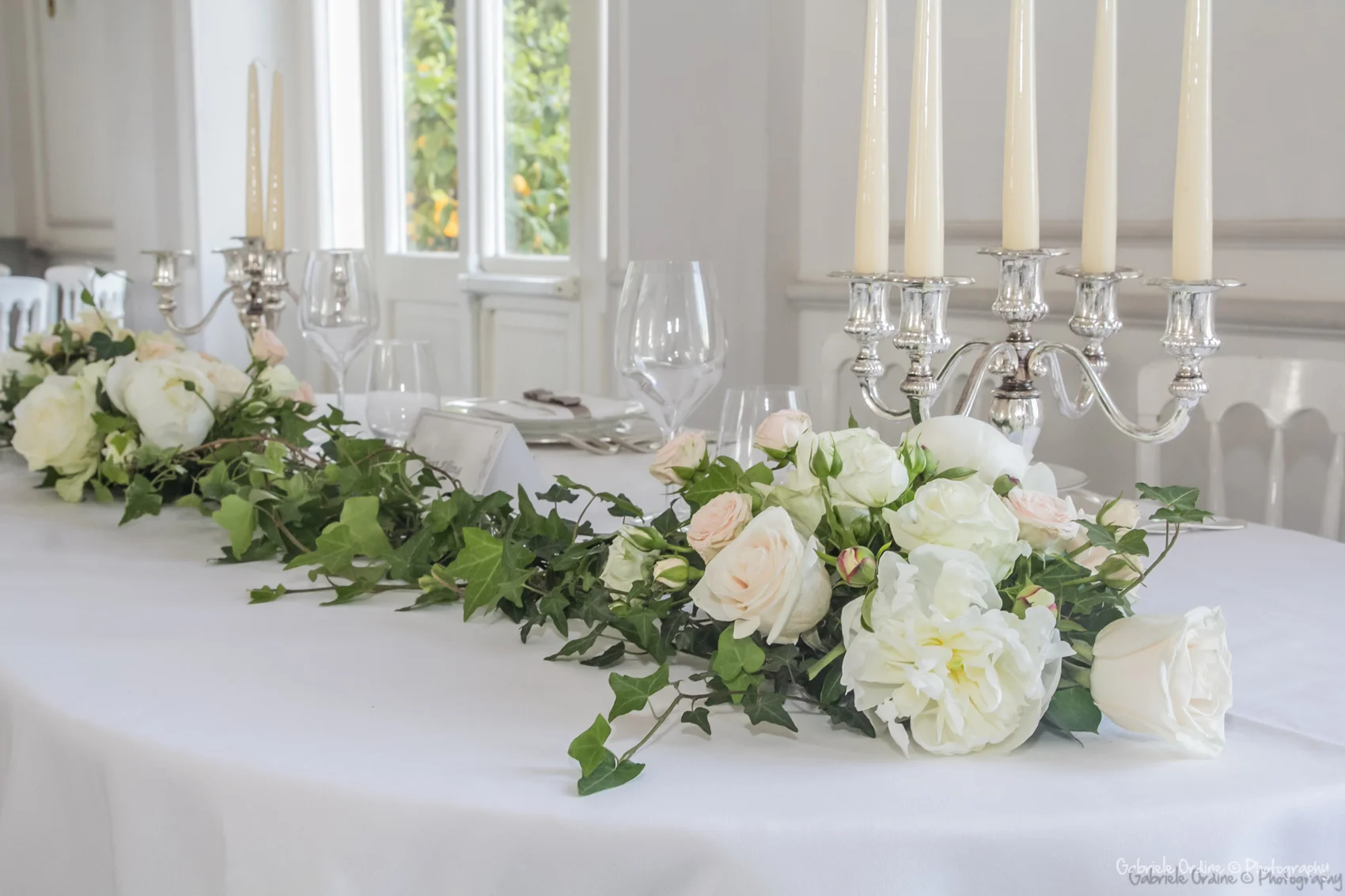 Centrotavola di rose bianche ed edera su un tavolo con candelabri d’argento