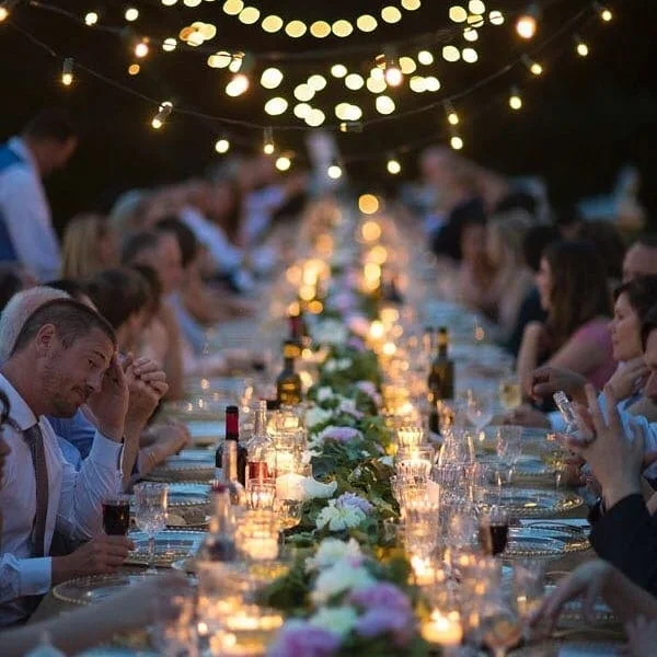 Lunga tavolata illuminata da candele e luci sospese durante la cena di nozze